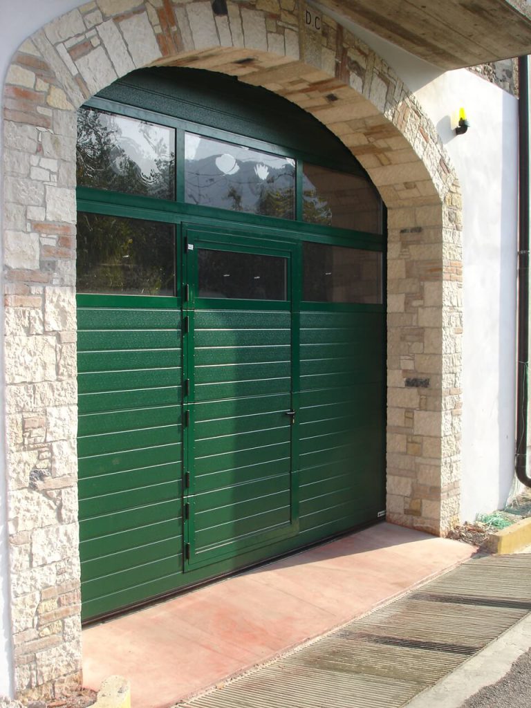 Porta per garage sezionale verde con porta pedonale e oblò per rendere luminosi i tuoi spazi